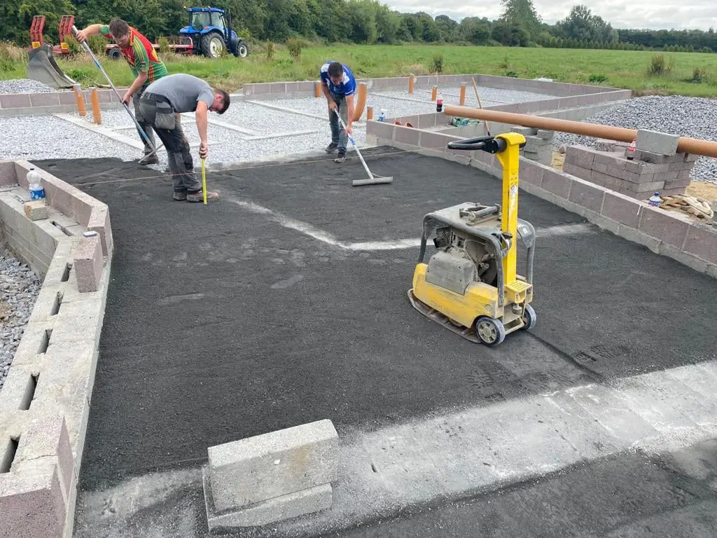 Workers levelling hardcore on a new foundation with a plate compactor